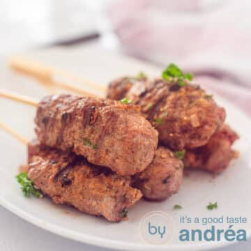 A square photo with five skewers of kefta kebab on a white dish. A white background.