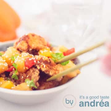 A square photo with a gray dish filled with crispy pork tenderloin in a sweet and sour sauce. Two chopsticks grab a block of meat