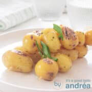 A square photo with a white plate with three baby potatoes skewers with spring onions. A white background