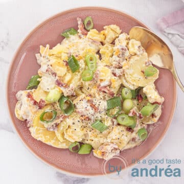 A pink plate photographed from above with potato salad with Cheddar and Bacon.