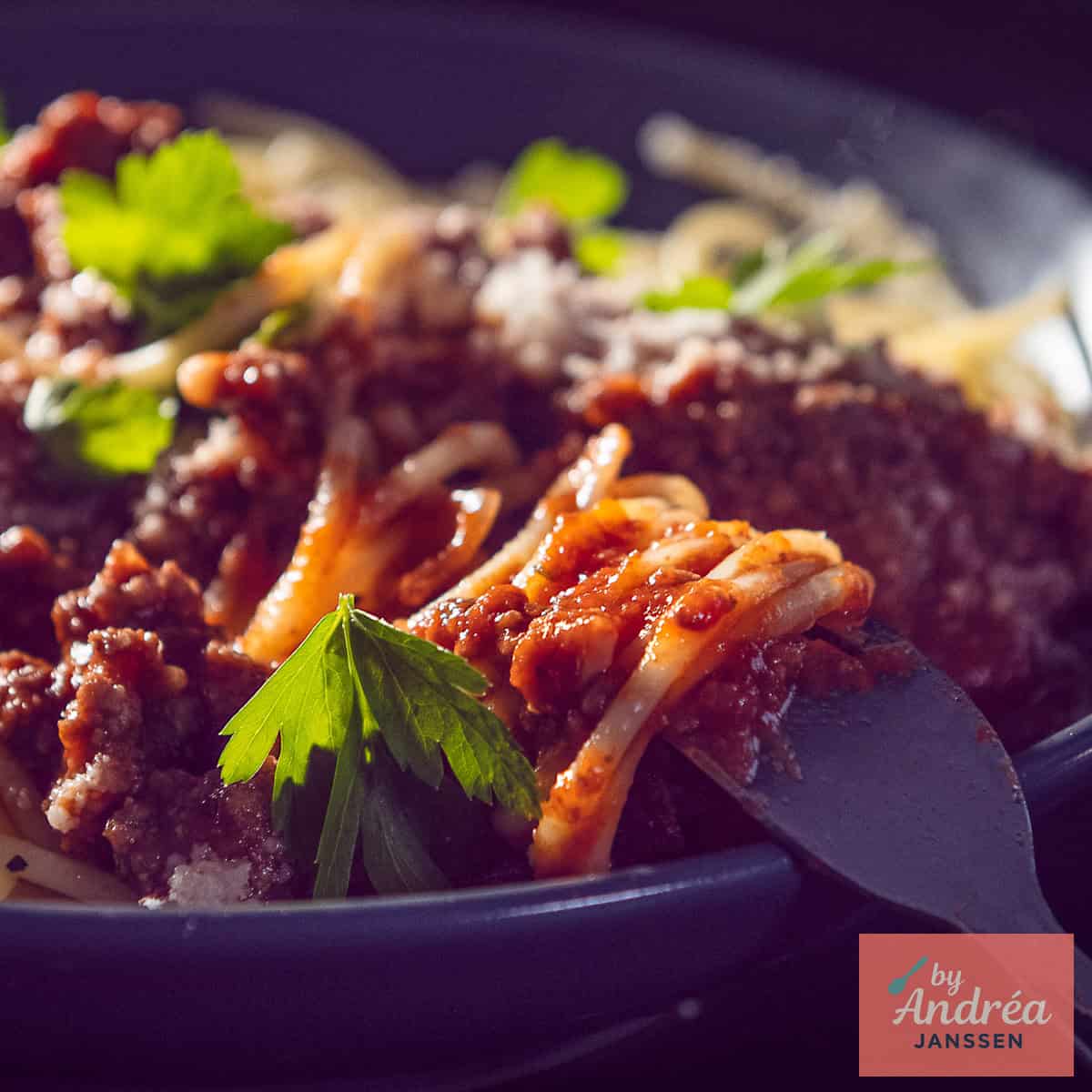 A square photo of a plate of spaghetti with bolognese sauce in it.