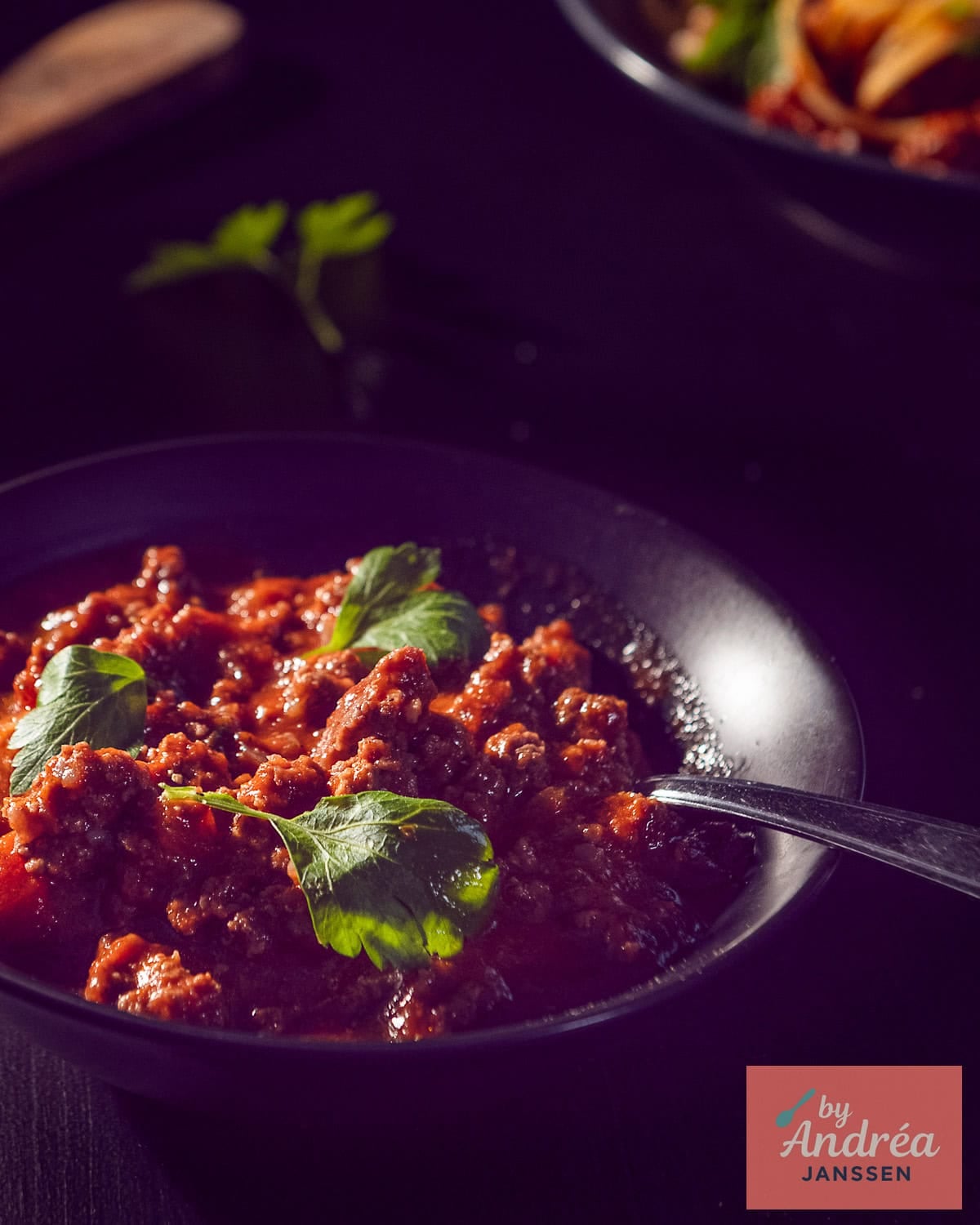 A black bowl with bolognese sauce and a parsley garnish