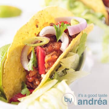 A taco filled with chili without beans. With a topping of onions and parsley on a white background