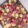 A baking tray, not yet baked, with pommes duchesse, various vegetables and pieces of beef finch on a white surface.