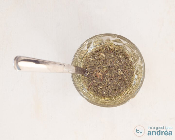 A glass with herbal oil of olive oil, thyme and rosemary. A spoonful in it.