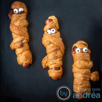 A square photo with three frankfurter mummies in puff pastry on a black background for Halloween