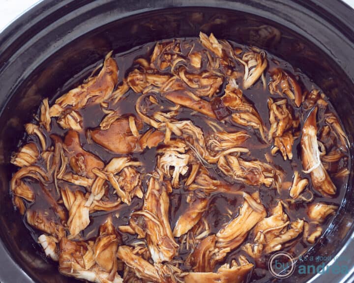 A slow cooker filled with pulled chicken.