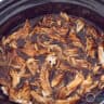 A slow cooker filled with pulled chicken.