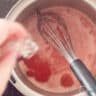 A saucepan with strawberry sauce in which gelatin is dissolved.