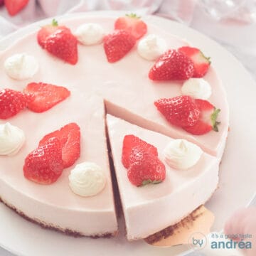 A square photo with a strawberry cheesecake with a point cut out. Garnished with fresh strawberries and whipped cream.