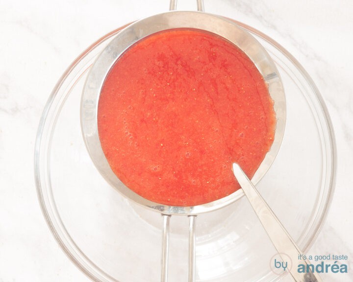Strawberry pulp is sieved over a glass bowl