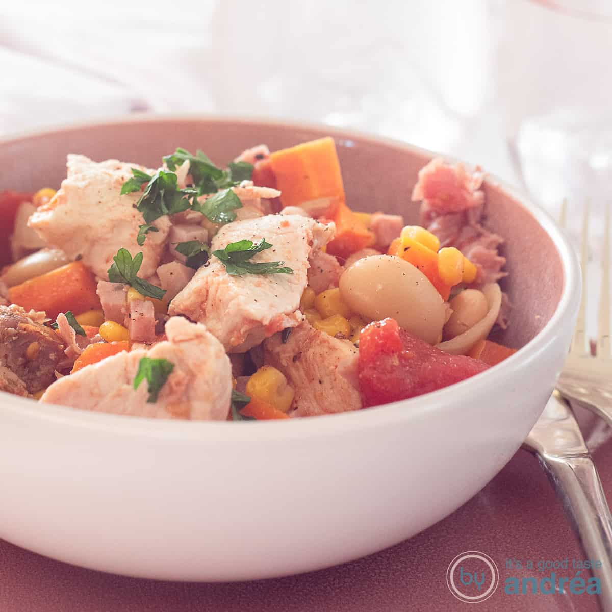 A square photo with a pink bowl filled with slow cooker Brunswick stew. Very colorful!