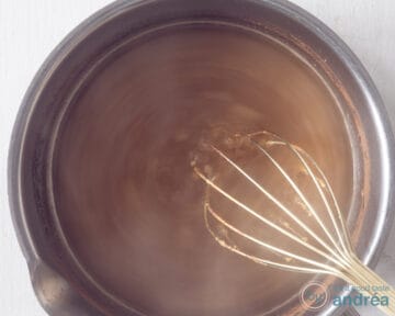 Orange honey glaze in a saucepan. A whisk is in the pan