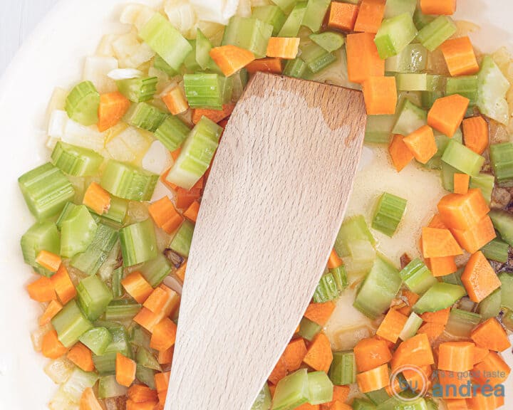 A white frying pan in which celery, garlic, carrot and onion are fried