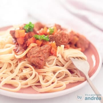 A square photo with a pink plate with tagliatelle and Italian stew