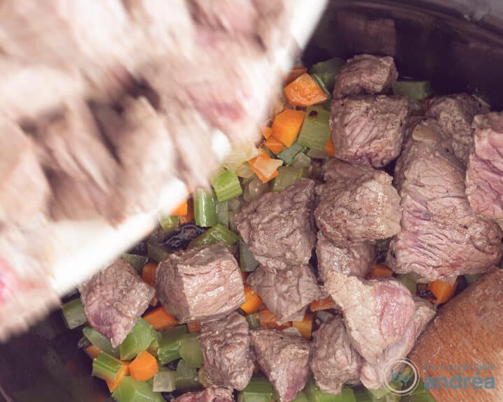 The fried meat is spooned onto the vegetable mix in the slow cooker.
