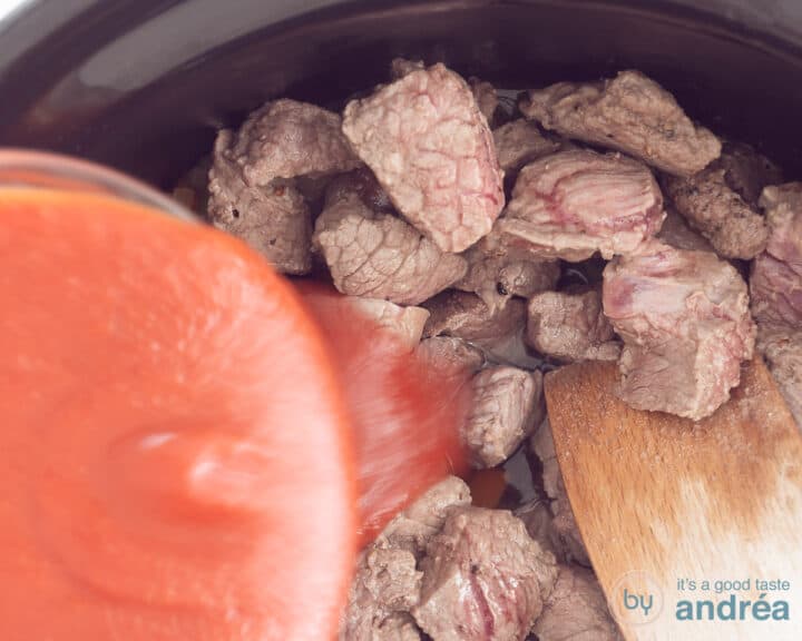 In the slow cooker, the sieved tomatoes are poured over the meat mix
