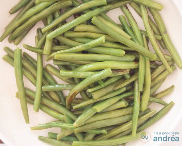 A white frying pan in which green beans are stir-fried.