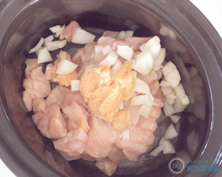 A slow cooker with chicken cubes, chicken, garlic and onion.