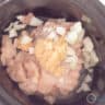 A slow cooker with chicken cubes, chicken, garlic and onion.