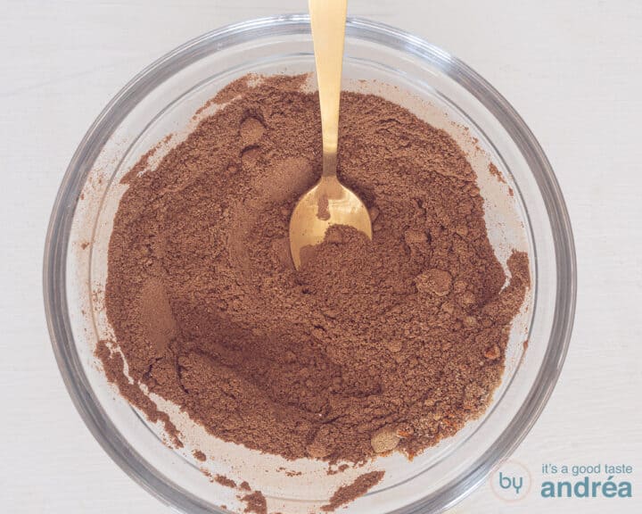 A glass bowl with a spice mix. A golden spoon lies inside.