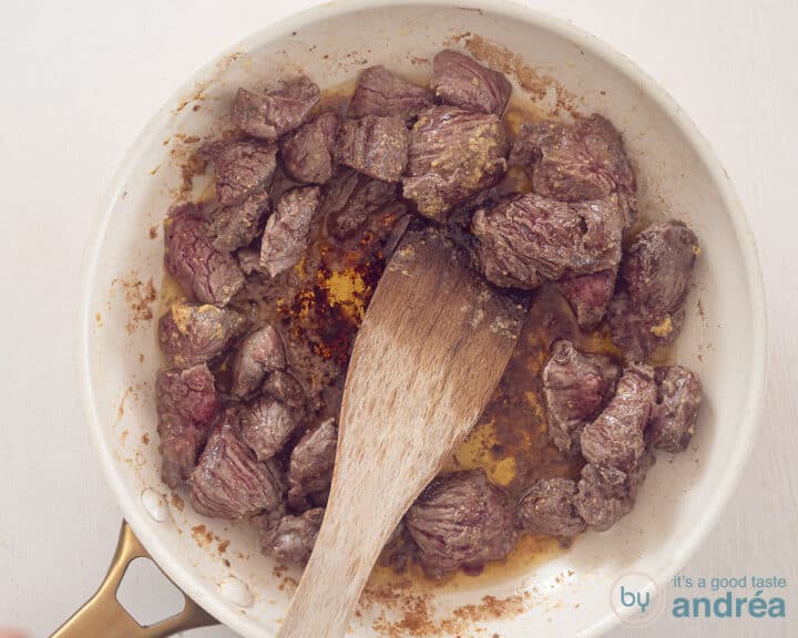 A white frying pan in which beef has been fried