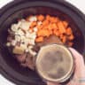 A slow cooker filled with meat, parsnips and carrot cubes. Beer is served