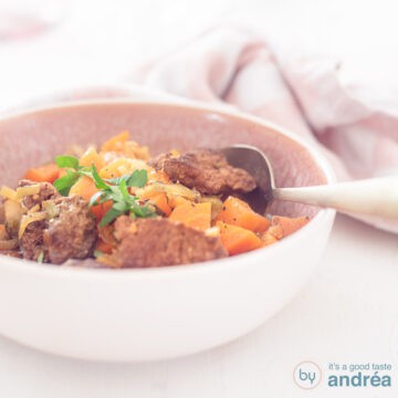 A square photo with a pink bowl filled with beef stew with winter vegetables in a beer broth sauce on a white background.