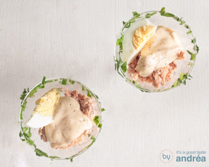 Two glasses from above with a parsley rim filled with salmon, capers, whiskey sauce and an egg