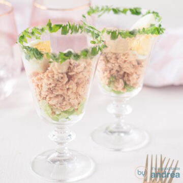 A square photo with two cocktail glasses filled with salmon, whiskey sauce and an egg. The rim of the glass at the top is garnished with parsley.