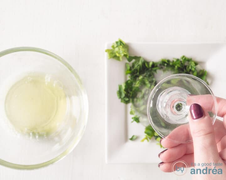 A bowl with egg whites and a plate with finely chopped parsley. A glass is pressed into the parsley.