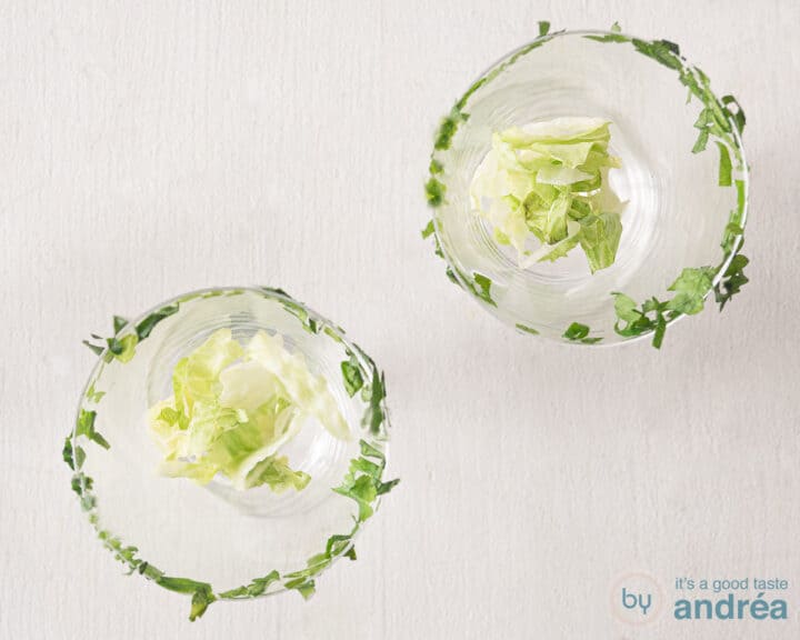 Two glasses on a white surface with a rim of finely chopped parsley. Fresh lettuce at the bottom of the glass.