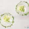 Two glasses on a white surface with a rim of finely chopped parsley. Fresh lettuce at the bottom of the glass.