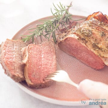 A square photo of roast beef with bacon, two slices of which have been cut off. A fork pierces a slice