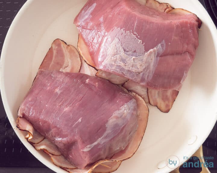 Roast beef covered with bacon that is fried in the frying pan.
