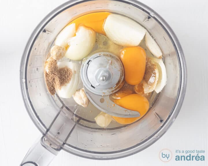 A food processor bowl with onion, garlic, candlenuts, cumin, coriander, turmeric, eggs and sugar.