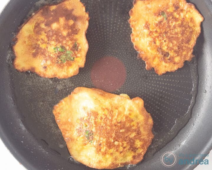Corn fritters are fried in a skillet until brown.