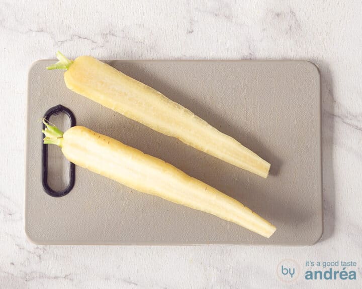 A gray cutting board with a halved carrot on it.