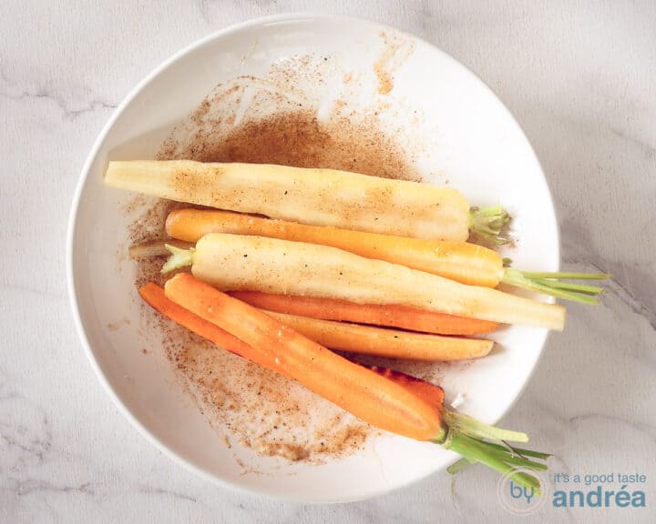 Marinating carrots with marinade in a white bowl.