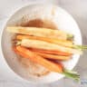 Marinating carrots with marinade in a white bowl.