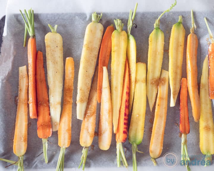 A baking tray filled with halved carrots with garam masala marinade.