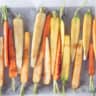 A baking tray filled with halved carrots with garam masala marinade.