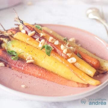 A square photo with a pink plate with colored carrots sprinkled with parsley and hazelnuts on a white surface.