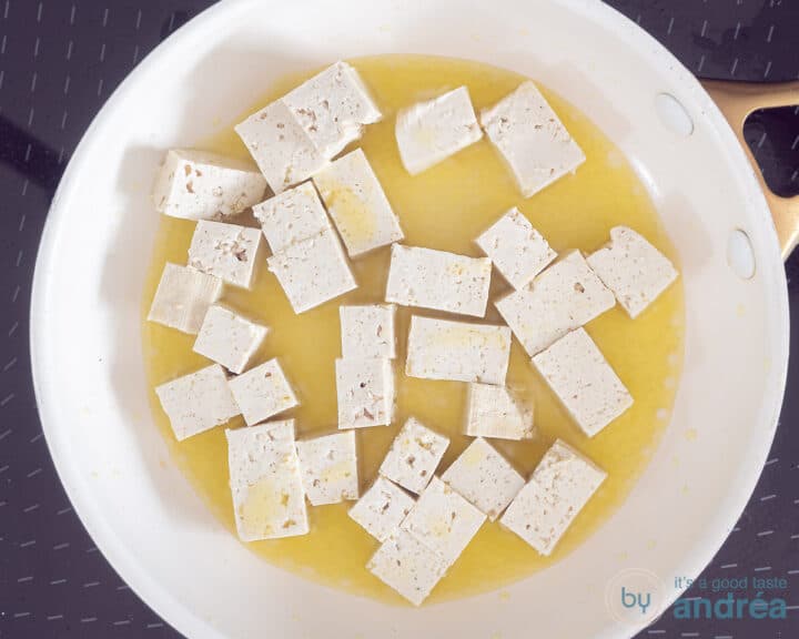 Tofu cubes fried in a white frying pan.