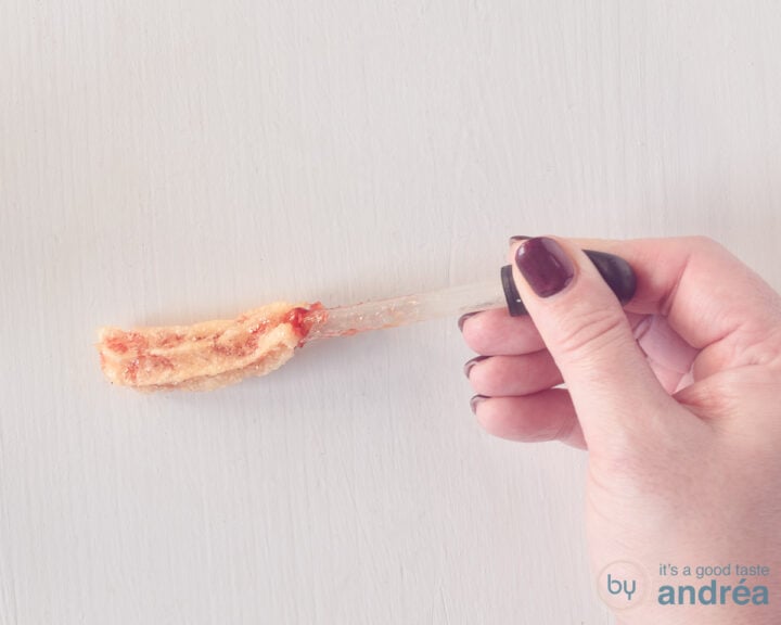 A churro on a white background, into which strawberry jam filling is injected with a pipette.