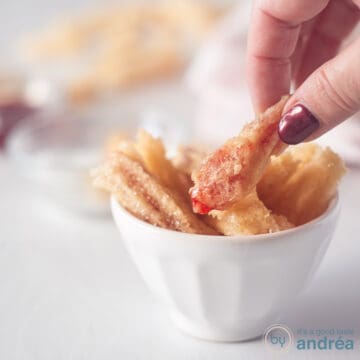 A square photo with a white bowl filled with strawberry churros. A hand grabbed a churro.