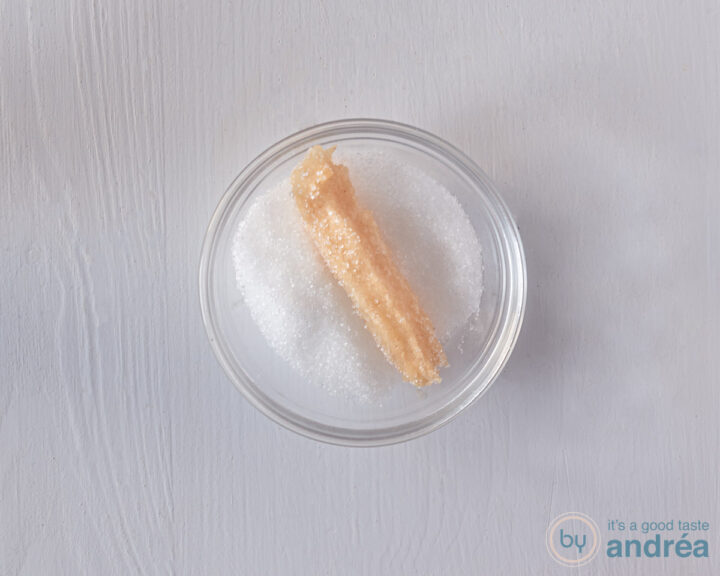 A glass bowl with sugar containing a churro.