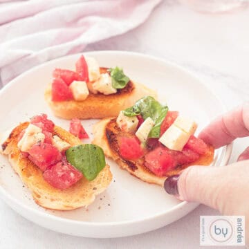 A square photo with a round white plate with three bruschettes with tomato, mozzarella and basil topping