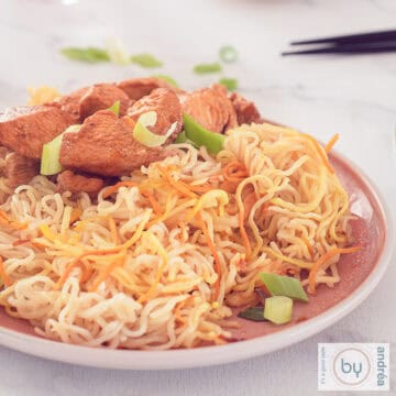 A square photo with a pink plate with noodles and cantonese chicken. A white background.