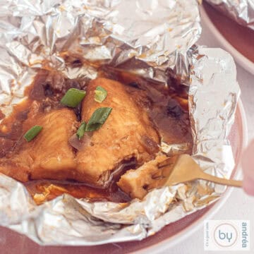 A square photo of a pink plate with unfolded aluminum foil containing pangasius fillet from the BBQ. A fork is poking a piece off.